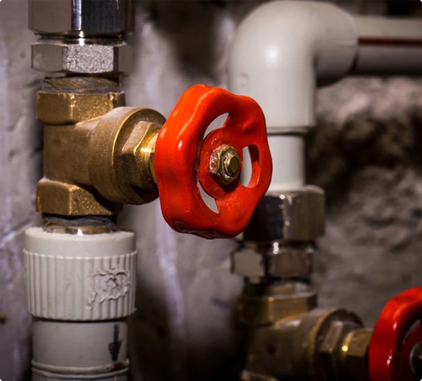 Close-up of a red valve handle on brass plumbing pipes.