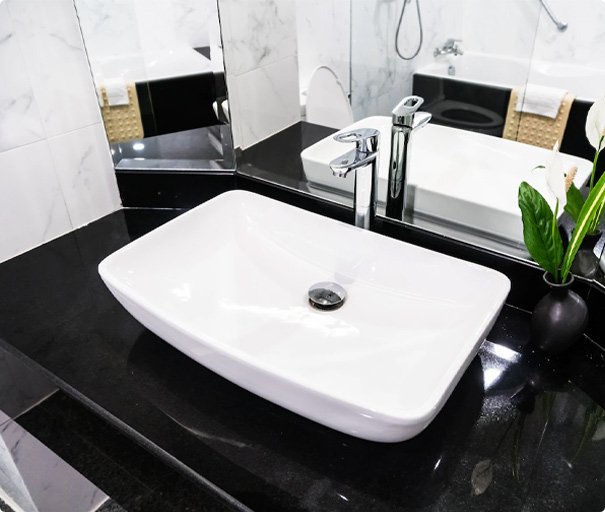 Modern bathroom sink with chrome faucet on black countertop.