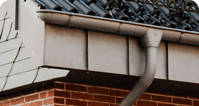 Close-up of a house roof with metal guttering and downpipe attached to a brick wall.