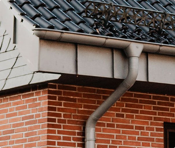 Close-up of a house roof with metal guttering and downpipe attached to a brick wall.